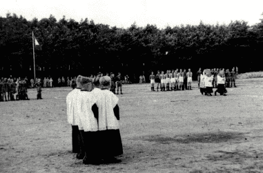 Gruppierung von Menschen in historischen Trachten auf einem Platz, im Hintergrund Uniformierte und eine Flagge.