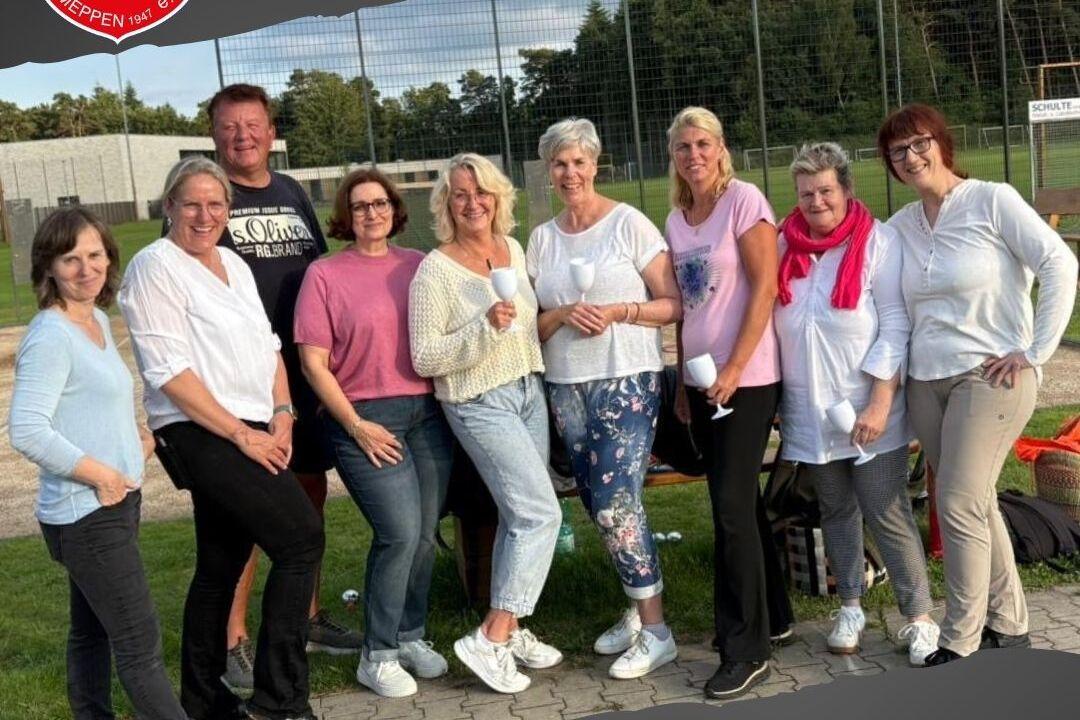 Gruppe von zehn Personen, l&auml;chelnd, vor einem Boulespielplatz, in sportlicher Kleidung zusammenstehend.