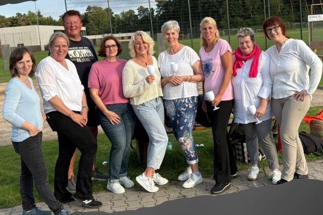 Gruppe von zehn Personen, l&auml;chelnd, vor einem Boulespielplatz, in sportlicher Kleidung zusammenstehend.