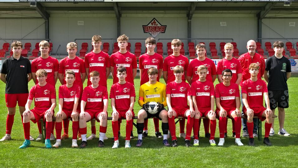 Teamfoto einer Jugendfu&szlig;ballmannschaft in roten Trikots mit einem Fu&szlig;ball, auf einem gr&uuml;nen Rasenplatz.