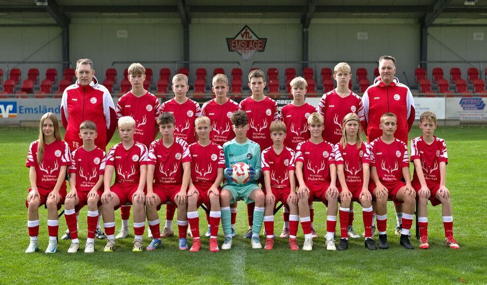 Mannschaftsfoto einer Jugendfu&szlig;ballmannschaft in roten Trikots, umgeben von Trainern auf einem Rasenplatz.