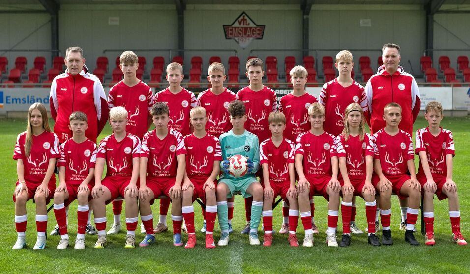 Mannschaftsfoto einer Jugendfu&szlig;ballmannschaft in roten Trikots, umgeben von Trainern auf einem Rasenplatz.