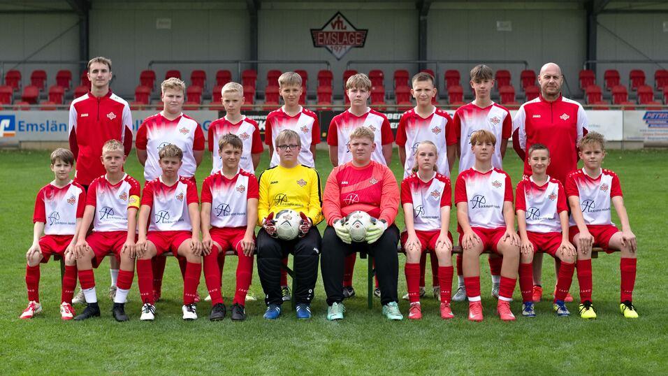 Gruppenfoto einer Fu&szlig;ballmannschaft mit 18 Spielern in roten Trikots und zwei Torwarten auf einem gr&uuml;nen Platz.