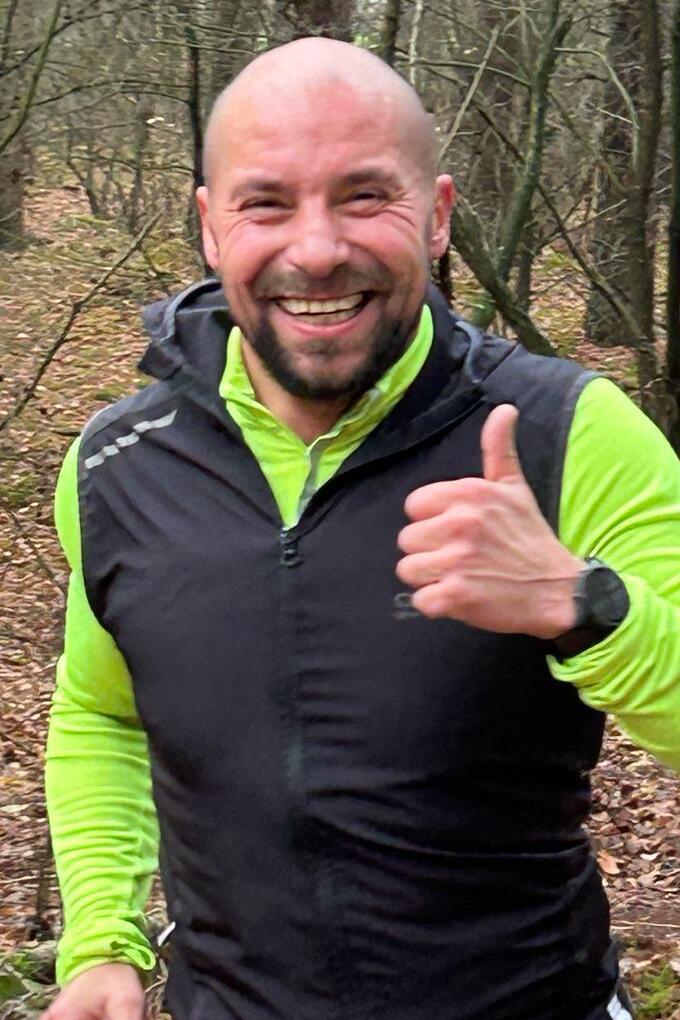 Ein fr&ouml;hlicher Mann in Sportkleidung gibt im Wald ein Daumen-hoch-Zeichen w&auml;hrend des Laufens.