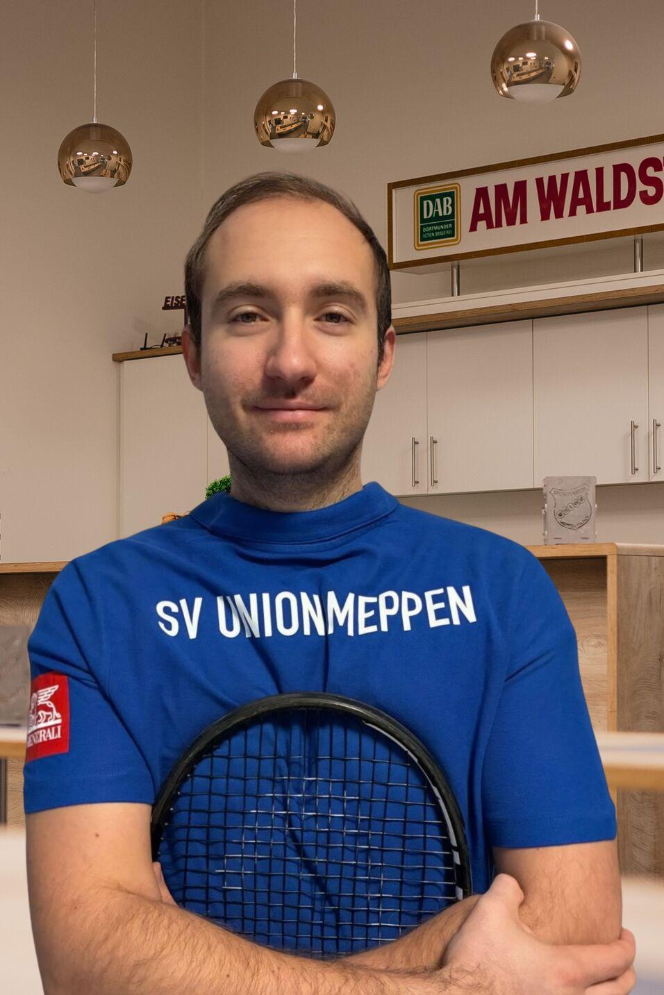 Portr&auml;t eines Mannes in blauer Sportkleidung mit Aufdruck &bdquo;SV UNIONMEPPEN&ldquo;, der einen Tischtennisschl&auml;ger h&auml;lt.