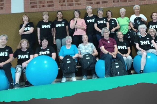 Gruppennahaufnahme von Frauen in Sportshirts, mit Gymnastikb&auml;llen im Hintergrund, w&auml;hrend einer Gymnastikstunde.