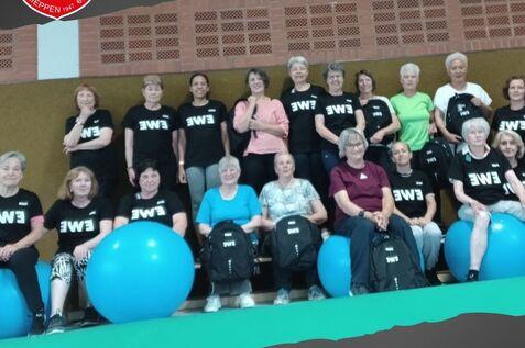Gruppennahaufnahme von Frauen in Sportshirts, mit Gymnastikbällen im Hintergrund, während einer Gymnastikstunde.