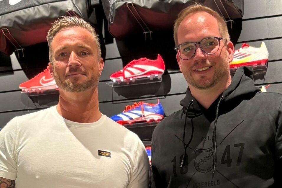 Zwei M&auml;nner stehen in einem Sportgesch&auml;ft und halten jeweils einen Jako-Fu&szlig;ball in der Hand. Im Hintergrund Schuhe.