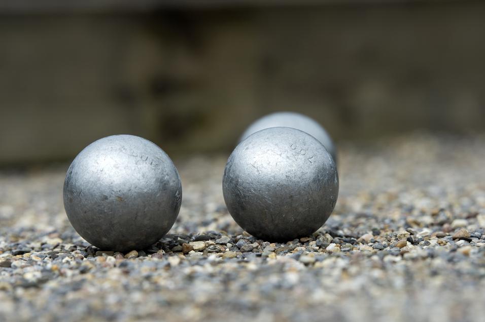 Vier silberne Boulekugeln liegen auf einem Kiesplatz, einige Kugeln sind im Vordergrund deutlich sichtbar.