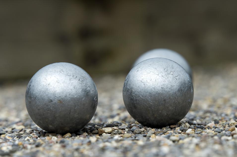 Vier silberne Boulekugeln liegen auf einem Kiesplatz, einige Kugeln sind im Vordergrund deutlich sichtbar.