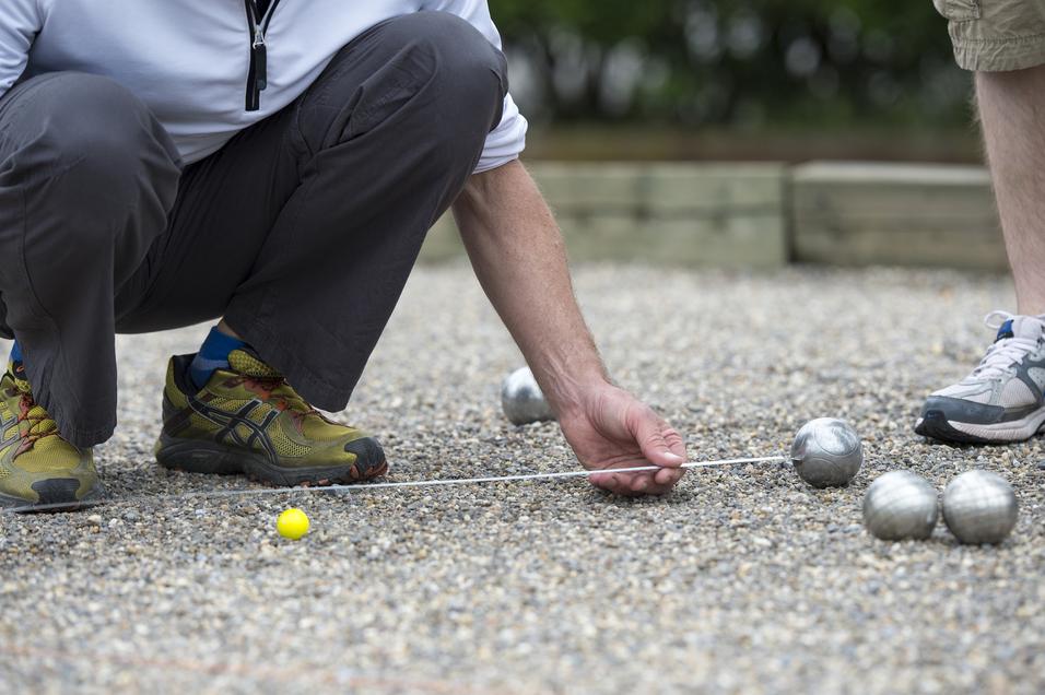 Nahaufnahme eines Spielers, der beim Boule-Spiel eine gelbe Kugel und silberne Kugeln in Kies untersucht.