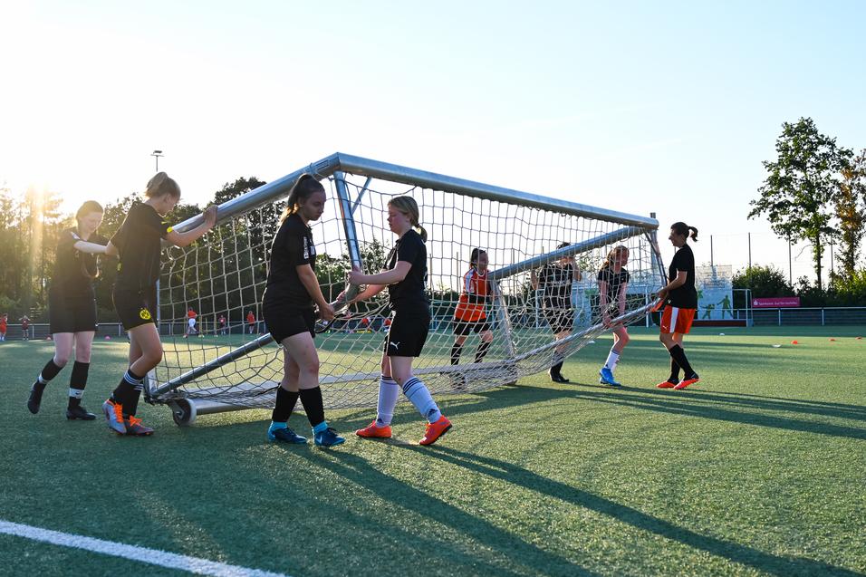Mannschaft von Fußballspielerinnen hebt ein Tor auf einem Kunstrasenplatz bei Sonnenuntergang an.