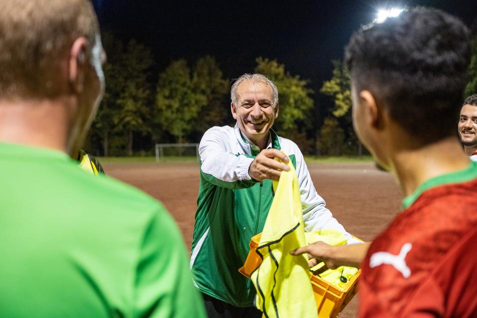 Trainer reicht gelbe Weste an Spieler während eines nächtlichen Fußballtrainings auf einem Platz.
